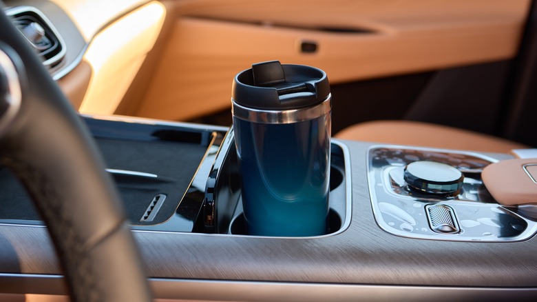 A coffee travel mug near a car's dashboard