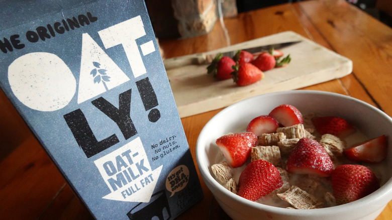 An Oatly oat milk container by a bowl of cereal with strawberries