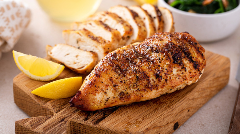 Whole and sliced chicken breast on wooden board