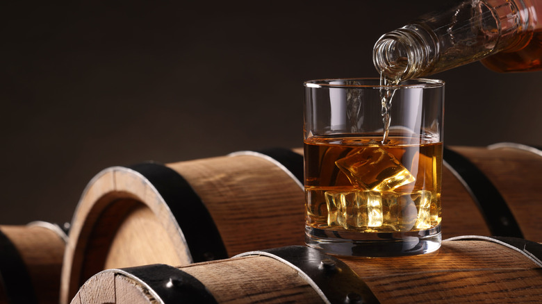 Bourbon being poured into a glass on top of oak barrel