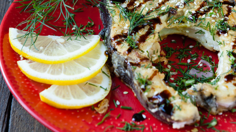 A grilled escolar steak on a plate with slices of lemon and herbs