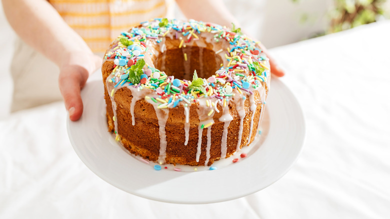 A round cake with a hollow center covered in icing and sprinkles
