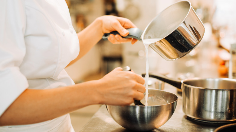 adding milk from a saucepan to a metal bowl