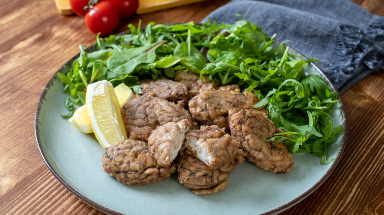 Fried pork brain with a greens salad sits on a blue plate on a wooden table