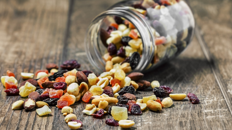 Trail mix with nuts and dried foods spilled on the floor from a half-full glass jar