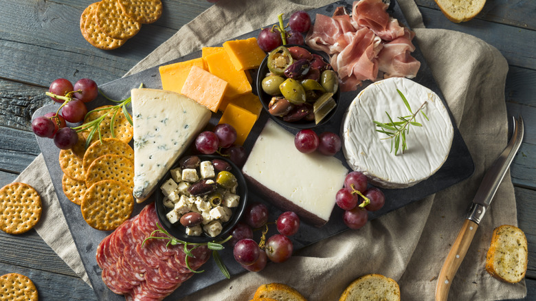 A cheese and charcuterie board with grapes, olives, and crackers