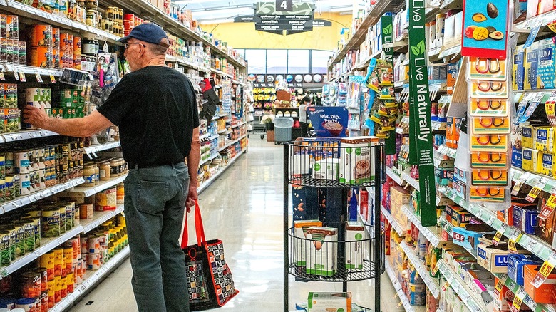 Man wearing blue baseball cap shopping for canned goods at Kroger