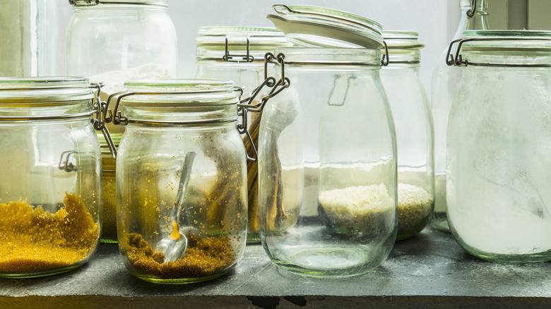 a series of mason jars on a shelf, two containing brown sugar and the rest empty