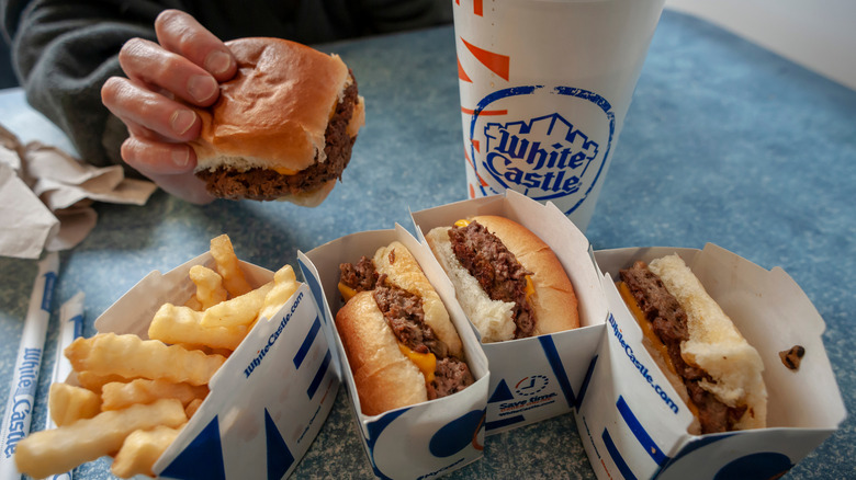 hand holding White Castle slider surrounded by other food items