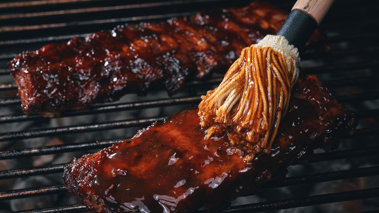 Babyback ribs on a charcoal grill are mopped with barbecue sauce