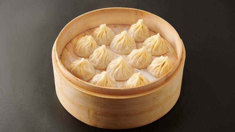 A bamboo steamer filled with soup dumplings against a gray background.