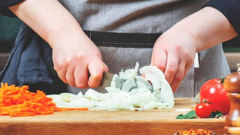 chef cutting onions on with a santoku knife.