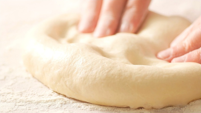 Close-up of fingers pressing into a ball of pizza dough
